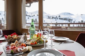 Une table à manger, dressée pour le repas, sur laquelle on trouve une variété de plats, notamment des viandes, des fromages et des légumes.