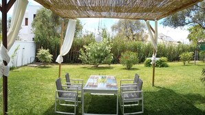 Une terrasse extérieure avec une table et des chaises, entourée d’une pelouse et de différentes plantes.
