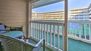 A balcony with wicker furniture, a view of a multi-story building with balconies, and a tennis court. - Pools, Tennis + Beach Access: Hilton Head Escape! (Hilton Head Island)