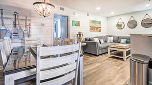 A modern living room with a glass-top dining table, grey sofa, and wooden flooring. - Pools, Tennis + Beach Access: Hilton Head Escape! (Hilton Head Island)