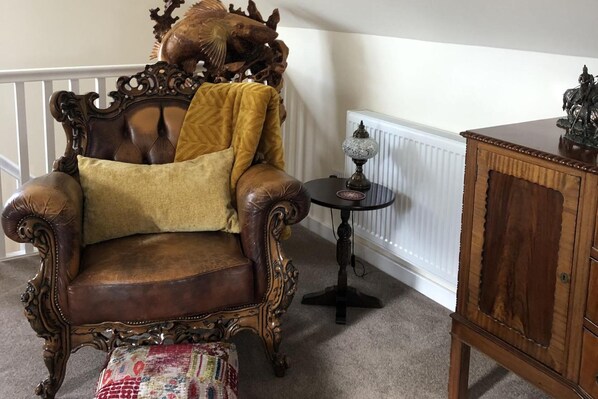 A traditional armchair with a decorative headrest, a small round table with a lamp, and a wooden cabinet. - Country Retreat Sleeps 2 Near Cymyran Beach (Holyhead)