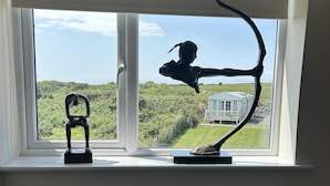 A window with two sculptures on the sill, overlooking a grassy area and a white building. - Country Retreat Sleeps 2 Near Cymyran Beach (Holyhead)