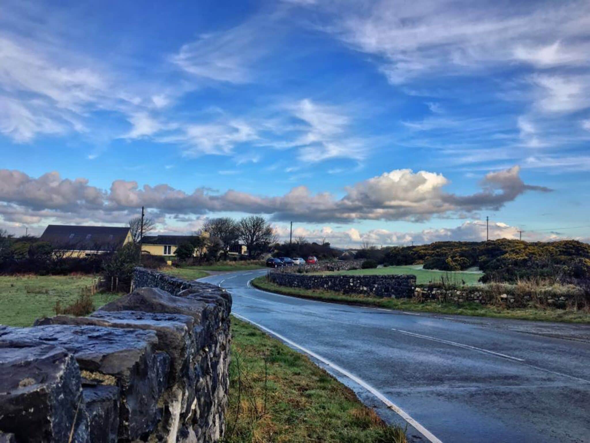 Eine ländliche Straße schlängelt sich durch eine Landschaft mit Steinmauern und saftigen Wiesen.