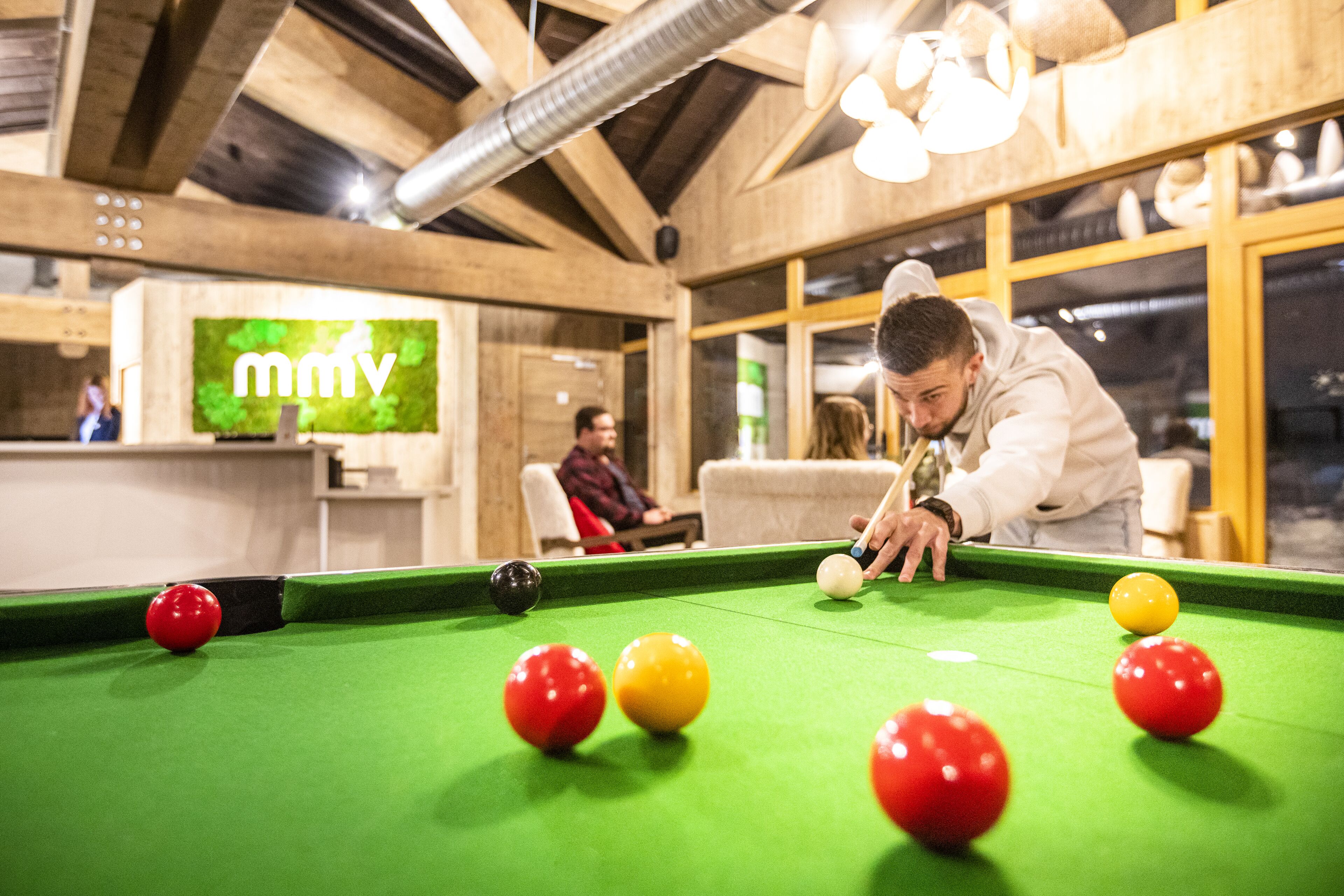 A pool table with balls, a person playing, and a 'mmv' sign in the background.