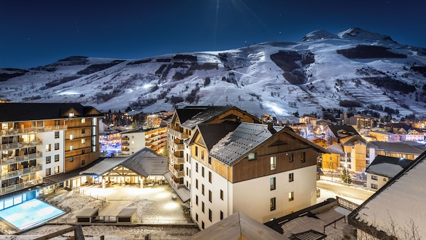 Una montaña nevada con una estrella brillante en el cielo. Se observan edificios con balcones y una piscina iluminada.