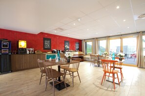 A modern restaurant with wooden tables and chairs, a red tiled wall, and large windows.