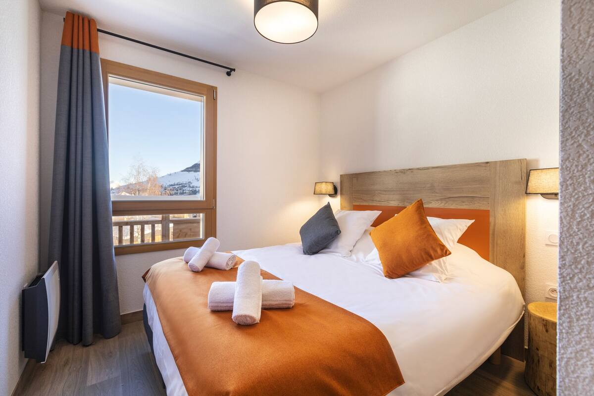 A hotel room with a bed, a window, a nightstand, and a lamp.