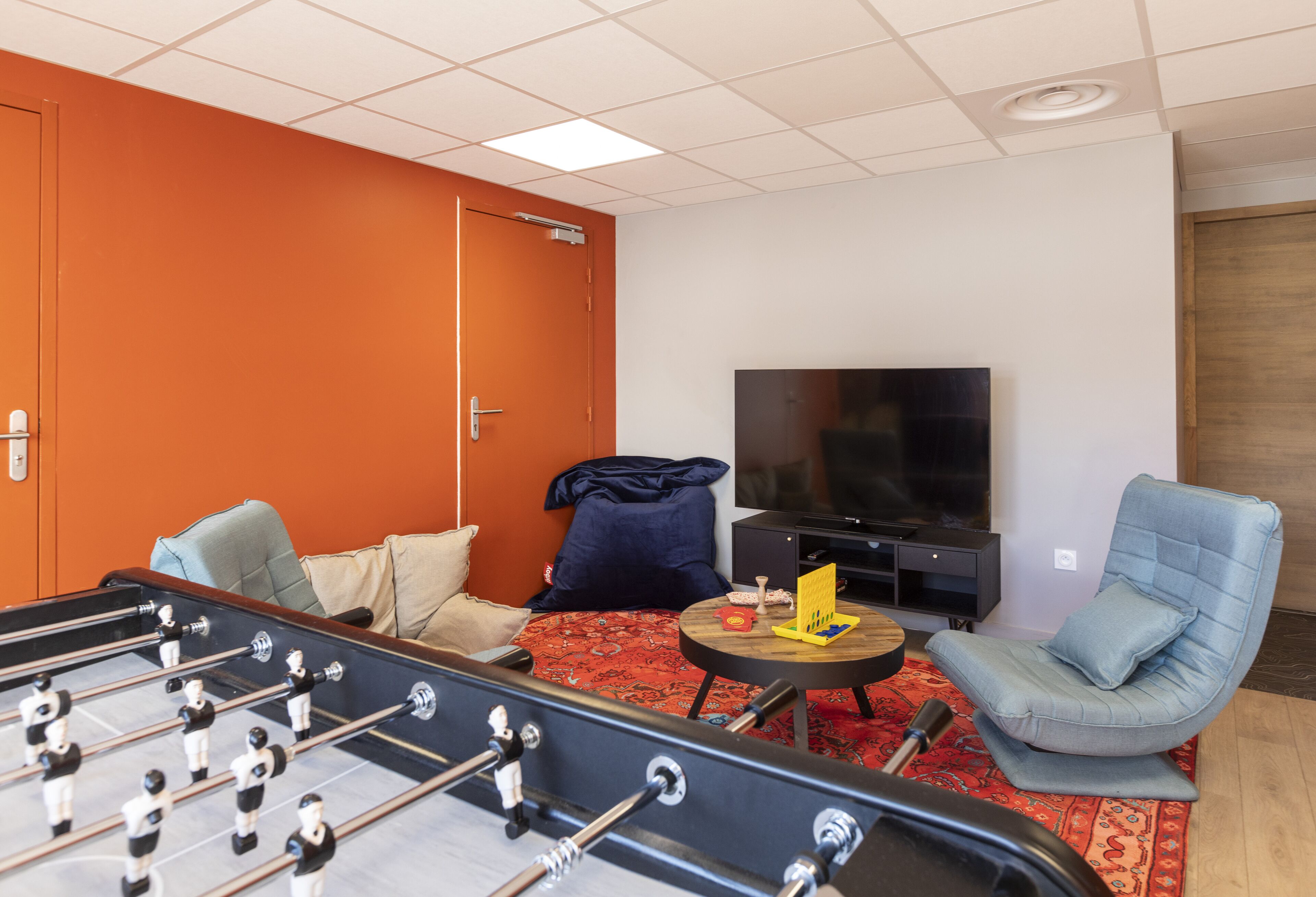 A room with a foosball table, a TV, a sofa, and a chair.