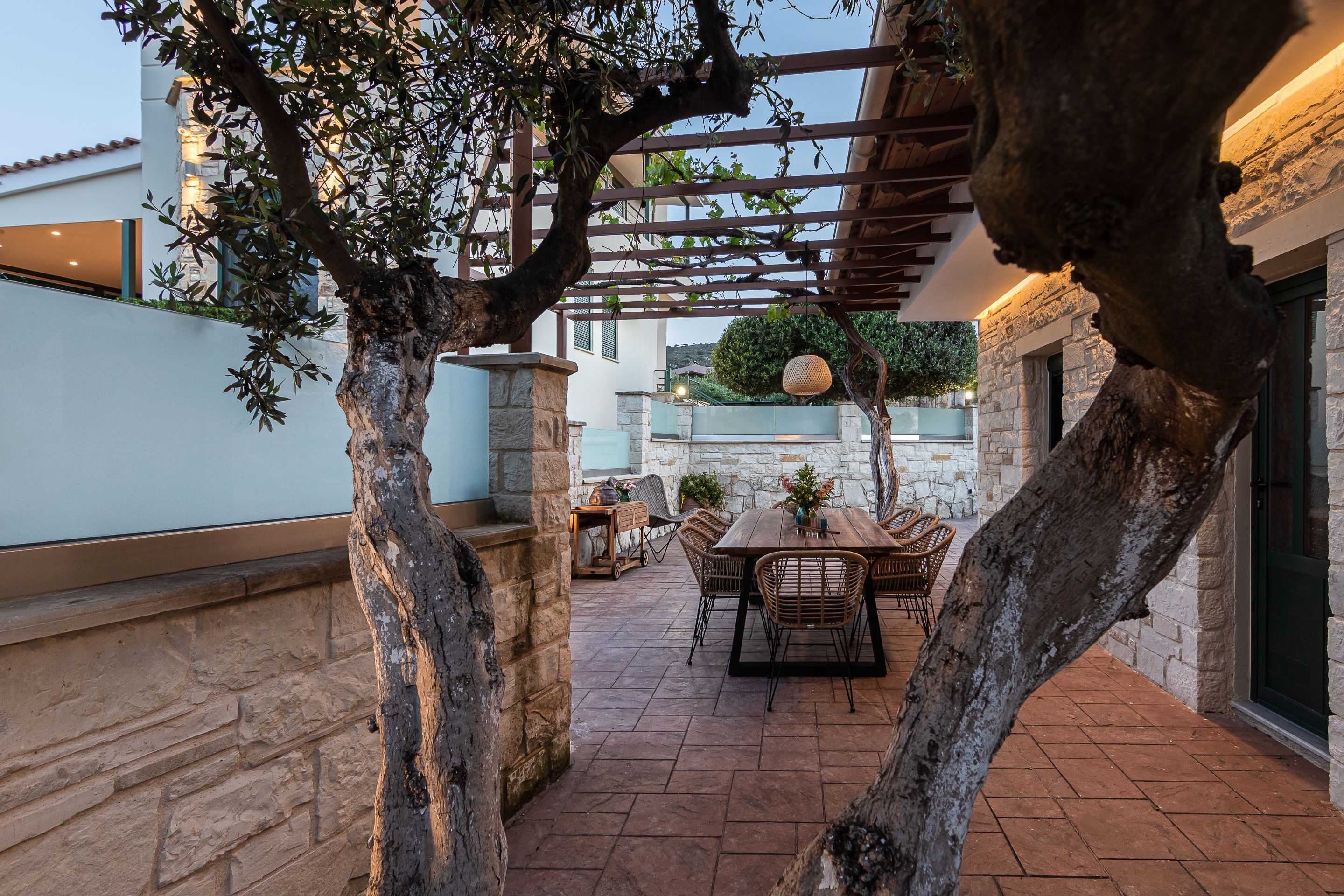 An outdoor patio with a pergola, stone walls, and a dining area with wicker furniture.