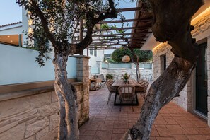 En uteplats med en pergola, stenmurar och en matplats med möbler av rotting.