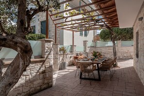En uteplats med stengolv, ett bord med stolar och en pergola.