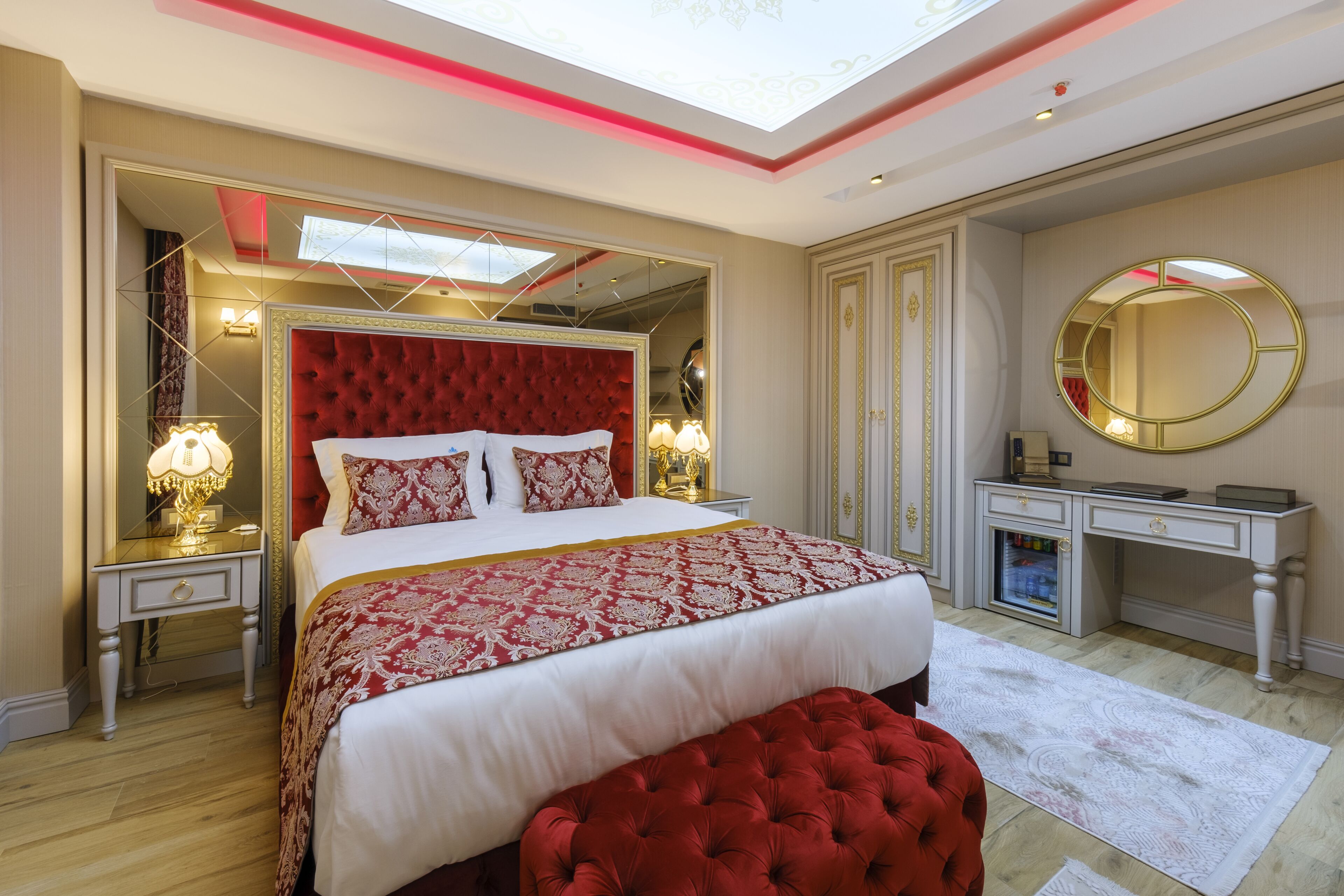 Een hotelkamer met een groot bed, een kaptafel met spiegel en een rode stoffen bank.