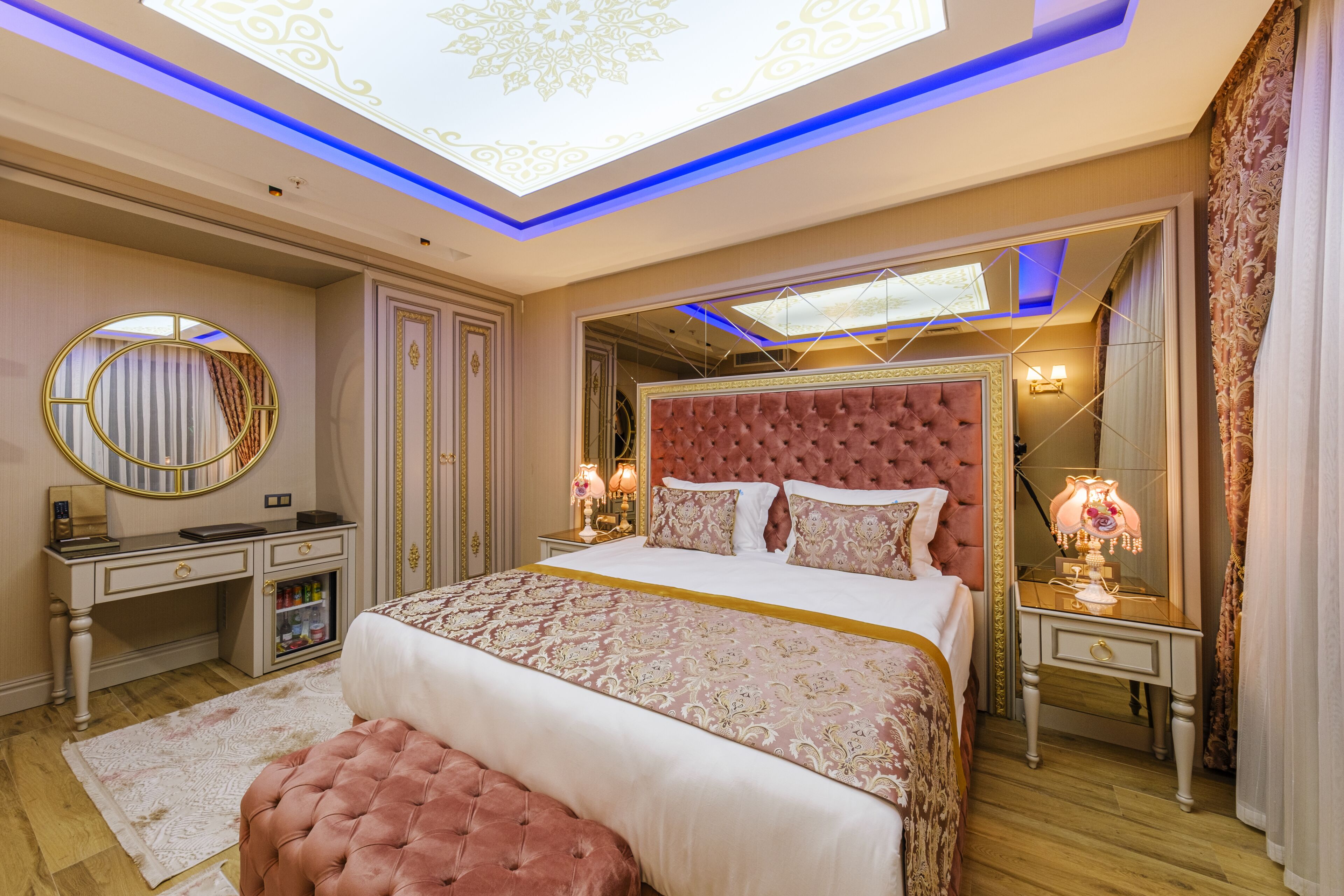 A luxurious bedroom with a large bed, a vanity with a mirror, and a desk with a lamp.
