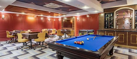 A pool table with a blue felt surface, surrounded by yellow chairs and a brown table.