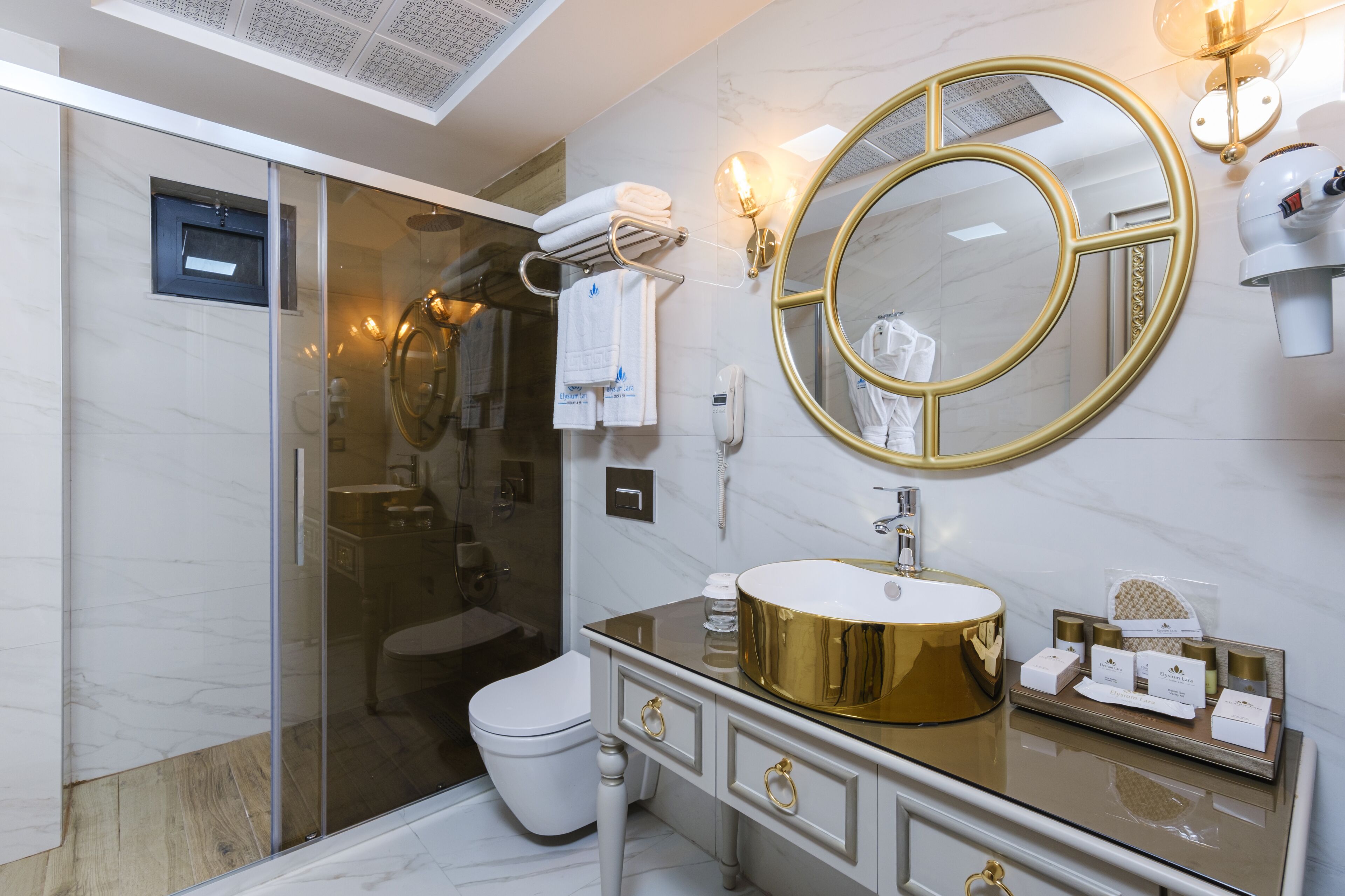 Un baño moderno con ducha envuelta en vidrio, tocador dorado y un espejo grande con marco dorado.