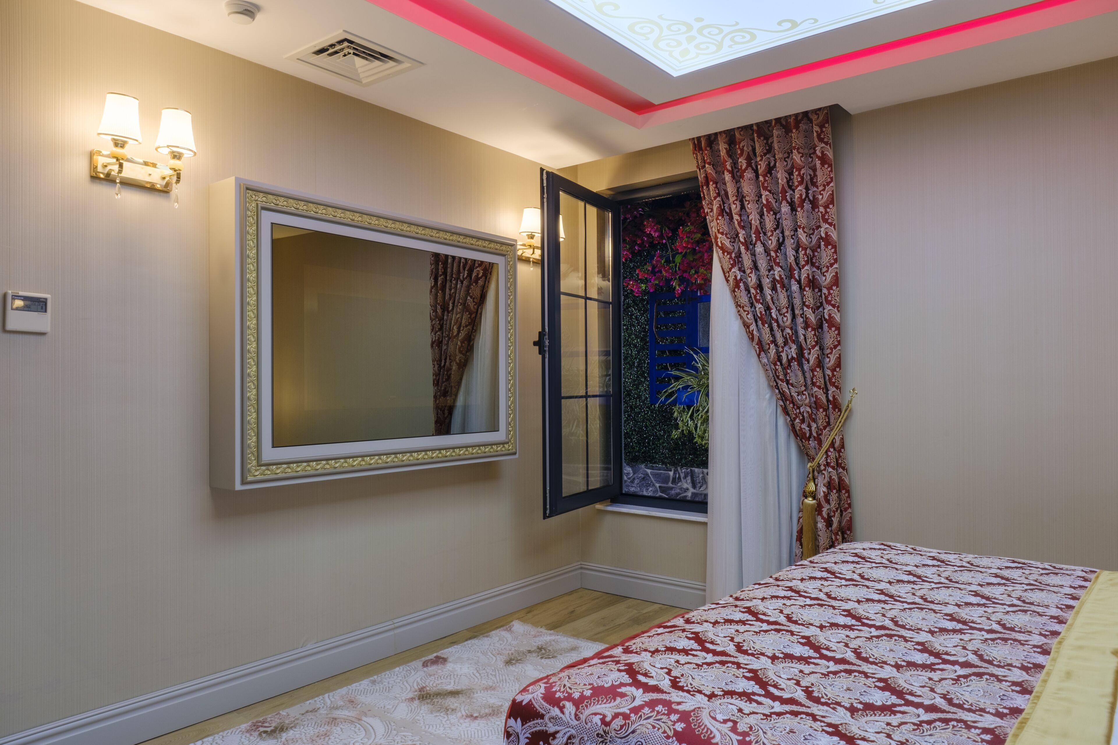 A bedroom with a large bed, a mirror, a window with curtains, and a skylight.