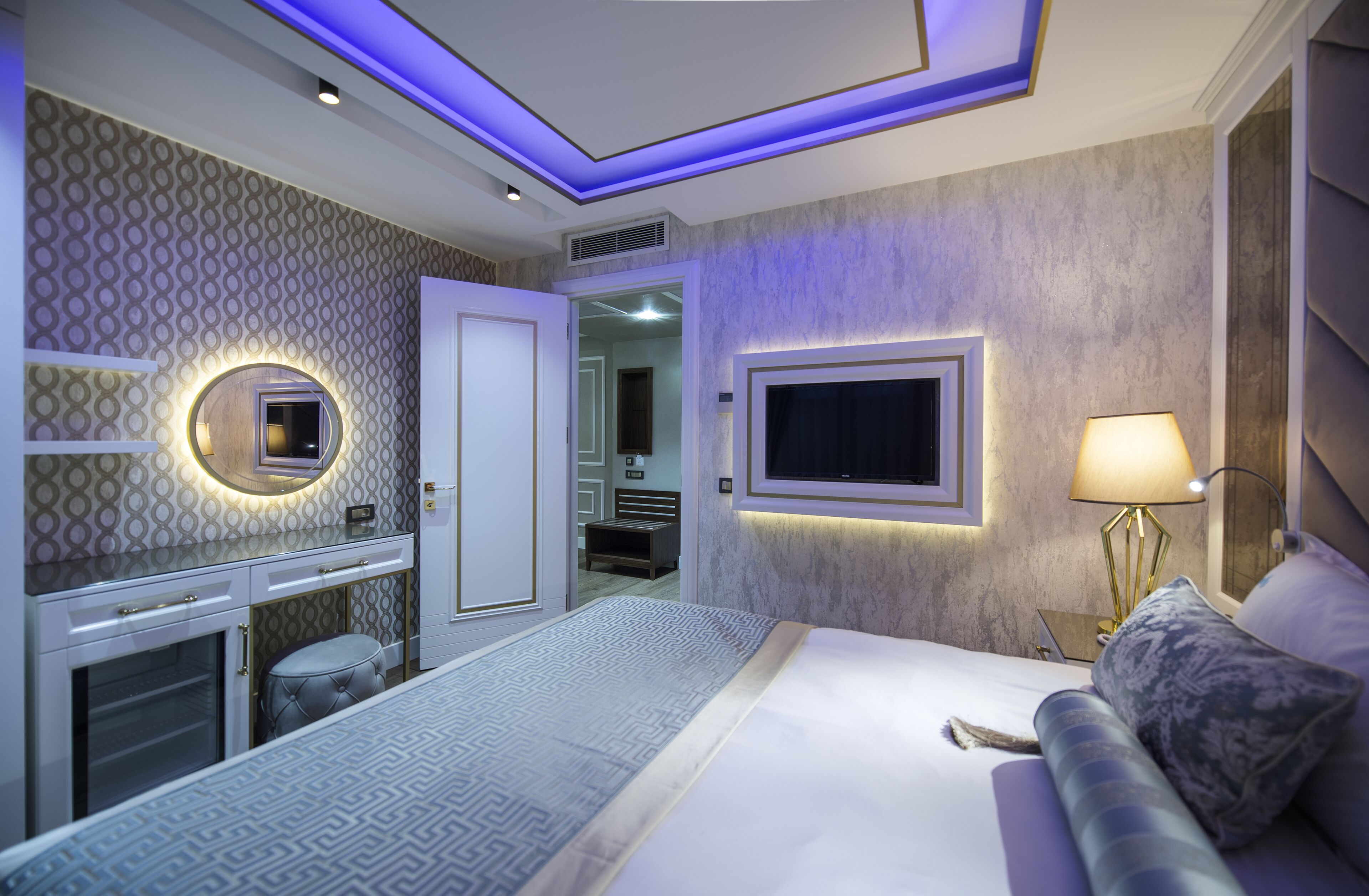 Una habitación de hotel moderna con una cama grande, un tocador con espejo, un televisor montado en la pared y una lámpara de noche.