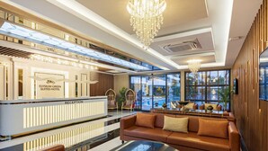 A modern hotel reception with a reception desk, seating area, and large windows offering views.