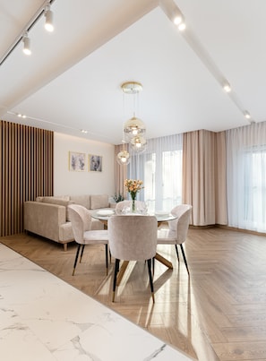 A spacious living area with a high ceiling, a dining table with chairs, a sofa, and a decorative vase with flowers.