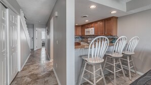 A modern kitchen with wooden cabinets, a microwave, and a bar area with white bar stools.