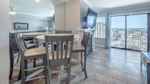 A modern kitchen with a dining area, a TV, and a view of the beach. - Here Comes The Sun #4 | Oceanfront + Pet-Friendly Townhome! (Carolina Beach)