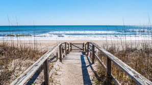 A wooden boardwalk leading to a beach with waves crashing onto the shore. - Here Comes The Sun #4 | Oceanfront + Pet-Friendly Townhome! (Carolina Beach)