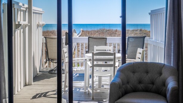 A deck with a view of the beach, white furniture, and a grey armchair. - Here Comes The Sun #4 | Oceanfront + Pet-Friendly Townhome! (Carolina Beach)