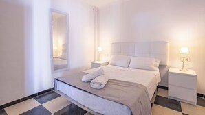 Une chambre d’hôtel avec un grand lit, deux tables de chevet avec des lampes, un miroir et un sol à carreaux.