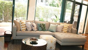 Ein modernes Wohnzimmer mit einem Ecksofa, einem runden Couchtisch und einem gestreiften Hocker.