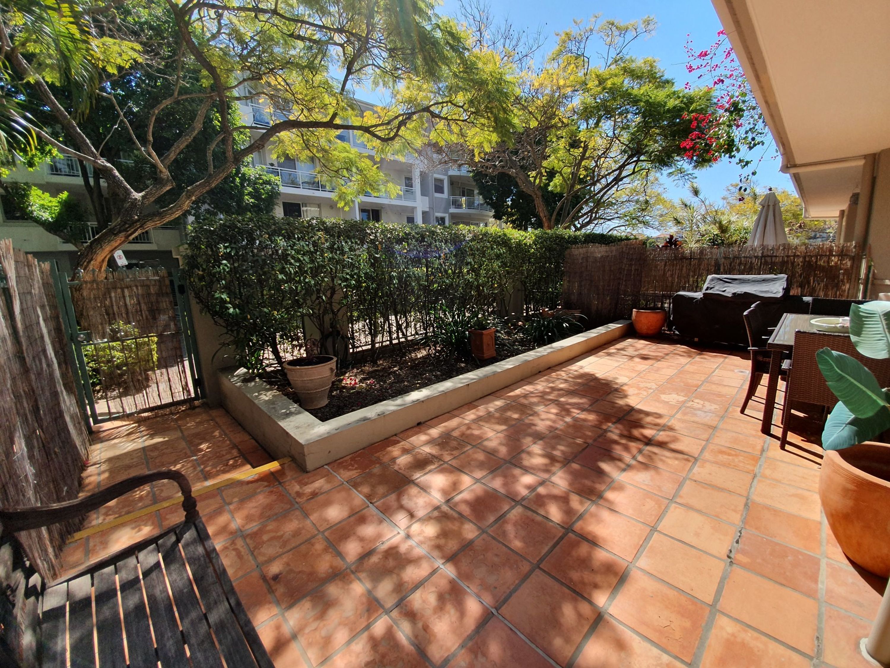Un patio con suelo de baldosas, una parrilla y plantas en macetas.