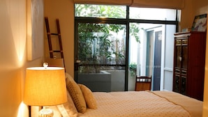 Ein Schlafzimmer mit einem Bett, einer Lampe, einem Fenster und Blick auf Grünflächen.