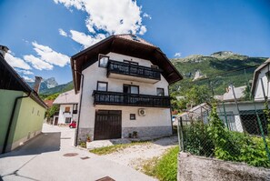 A two-story building with a balcony, a garage, and a mountain backdrop.