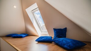 Ein Zimmer mit schrägem Dach, einem Oberlicht und einer hölzernen Bank mit blauen Kissen.