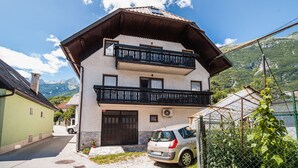 Ein zweistöckiges Gebäude mit Balkon, ein Auto davor und Berge im Hintergrund.