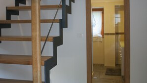 En trappe i træ med et moderne design, der fører op til et rum med flisegulv og en døråbning.