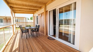 Een houten terras met een tafel en stoelen, een schuifdeur en een witte schutting.