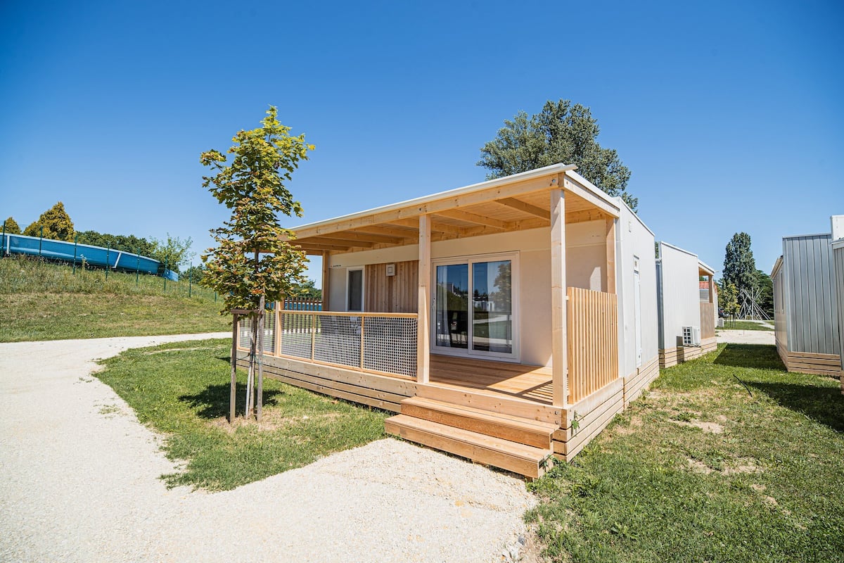 Een moderne stacaravan met een houten terras, grote schuifpuien en een omheind buitengebied.