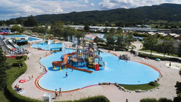 Een groot waterpark met diverse zwembaden en glijbanen, omgeven door groen en heuvels.