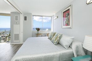 A bedroom with a large bed, a view of the sea, a painting on the wall, and a window with a view of the beach. - 11th Floor Waikiki Ocean, Lagoon & Marina Views! Walk to Beach! Washlet! (Honolulu)