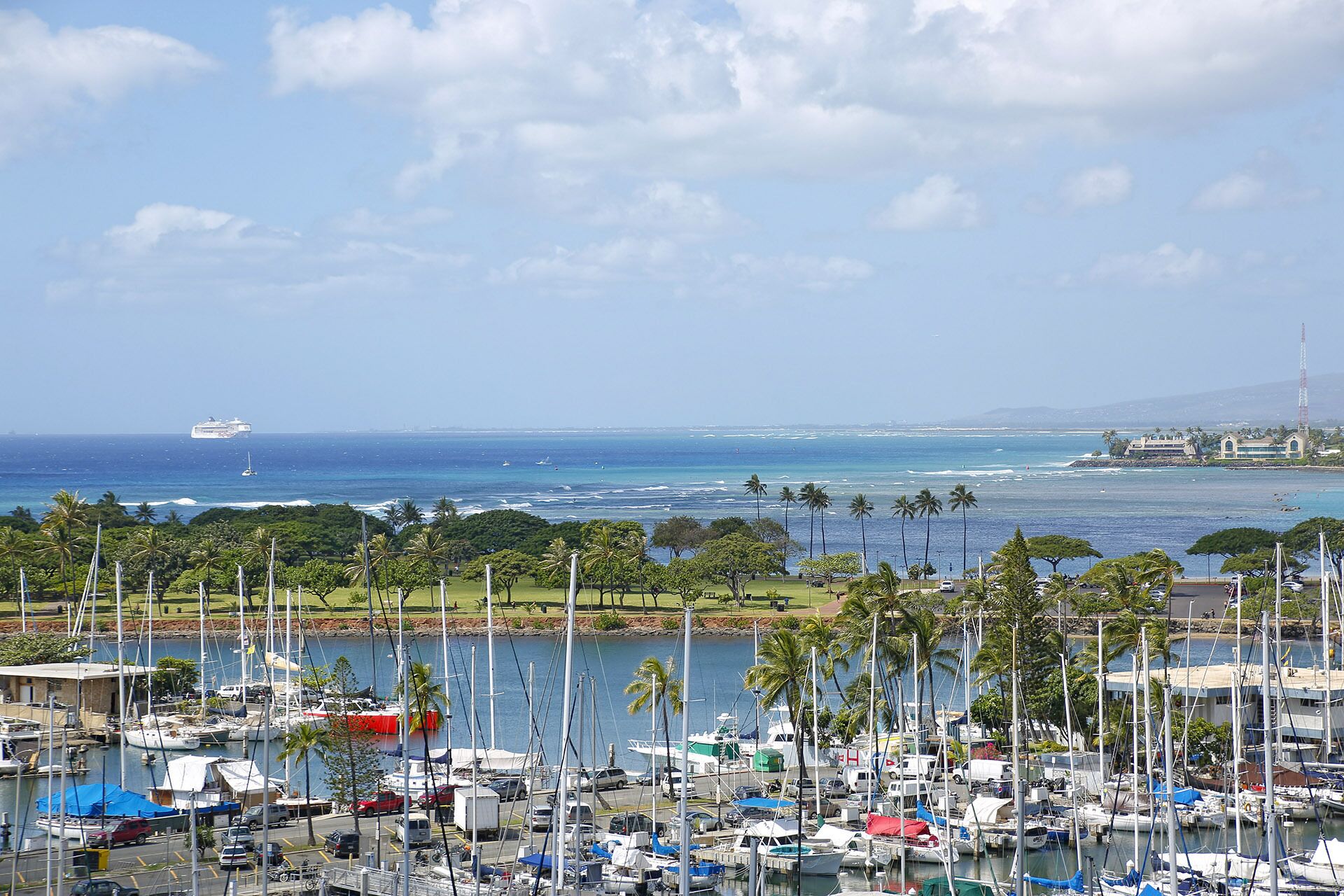 A marina with boats docked, a clear view of the ocean, and a distant cruise ship.