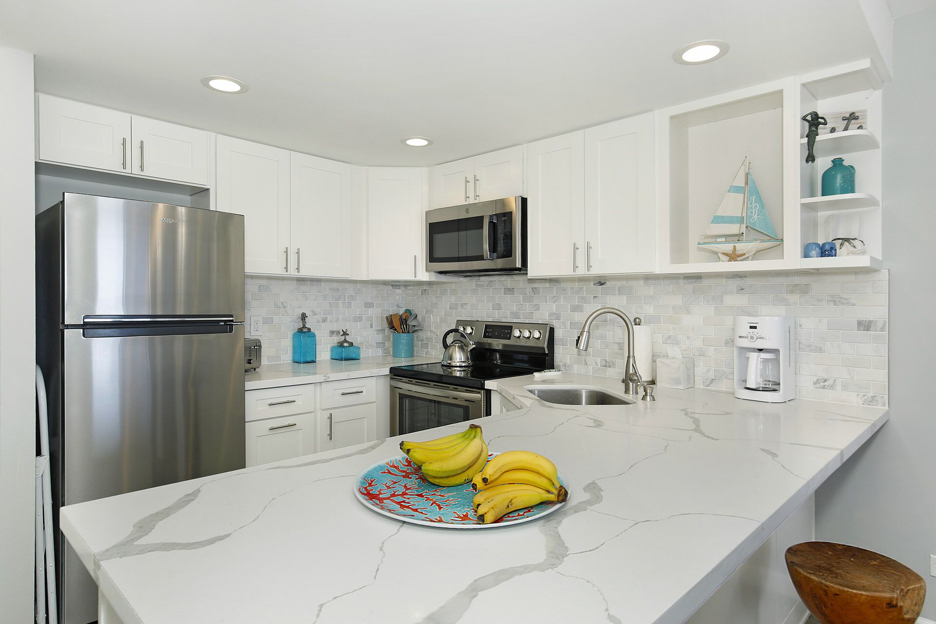 Een moderne keuken met witte kasten, roestvrijstalen apparatuur, een marmeren aanrecht en een bord bananen.