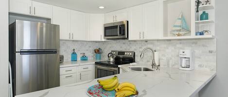 Een moderne keuken met witte kasten, roestvrijstalen apparatuur, een marmeren aanrecht en een bord bananen.
