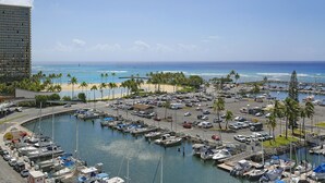 Ein Yachthafen mit vertäuten Booten, ein Strand mit Palmen und ein großes Gebäude im Hintergrund.
