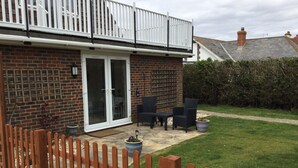 A brick house with a white balcony, a sliding glass door, and a patio area with outdoor furniture. - Holiday Let Annex; Self Contained; Sleeps 2; One minute from beach (Nr CHICHESTER)