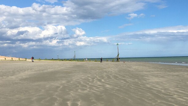 A wide sandy beach with gentle waves, a clear sky, and a few people in the distance. - Holiday Let Annex; Self Contained; Sleeps 2; One minute from beach (Nr CHICHESTER)