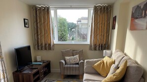 A living room with a sofa, armchair, TV, and a rug. - Holiday Let Annex; Self Contained; Sleeps 2; One minute from beach (Nr CHICHESTER)
