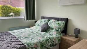 A neatly arranged bedroom with a bed, bedside tables, a desk, and a window with curtains. - Holiday Let Annex; Self Contained; Sleeps 2; One minute from beach (Nr CHICHESTER)