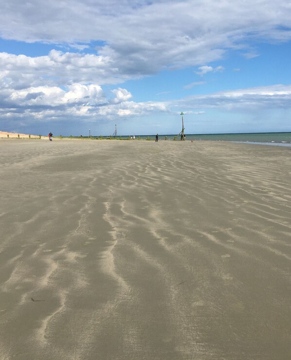 A wide sandy beach with gentle waves, a clear sky, and a few people in the distance.
