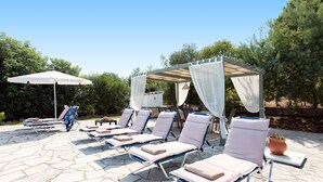 Un área junto a la piscina con sillas de descanso, una pérgola y una planta en maceta.
