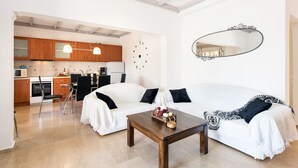 Una sala de estar moderna con un sofá blanco, una mesa de centro de madera y una cocina al fondo.